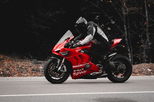 Free A rider in black gear speeds on a red Ducati motorcycle down a scenic highway surrounded by trees. Stock Photo