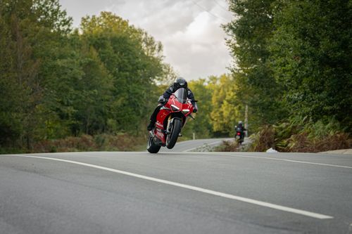 Free High-speed motorcyclist performing a wheelie on an open road surrounded by lush green forest. Stock Photo