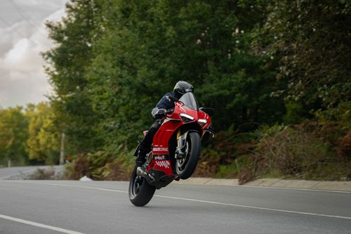 Free A dynamic shot of a red motorcycle executing a wheelie on a winding road surrounded by lush green trees. Stock Photo