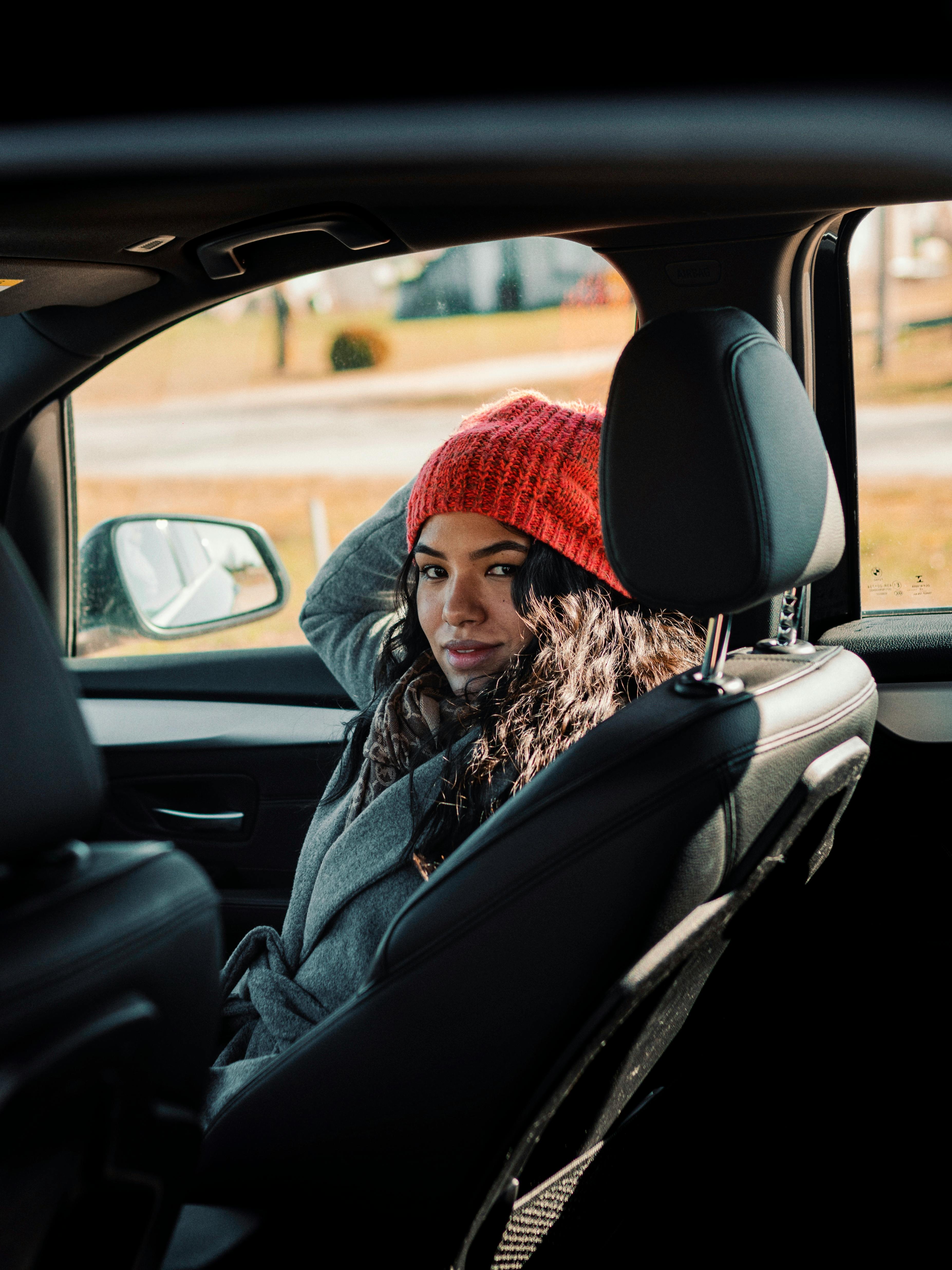 Woman in a red beanie relaxes in a convertible car seat, enjoying a sunny day.