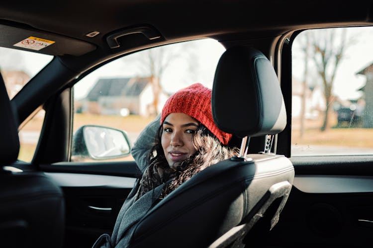 Woman In Grey Trench Coat And Red Knit Cap Sitting On Car Seat