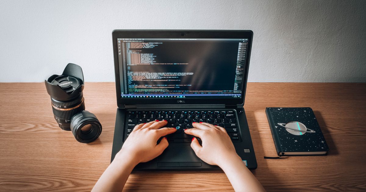 A web developer coding on a laptop at a wooden home-office desk