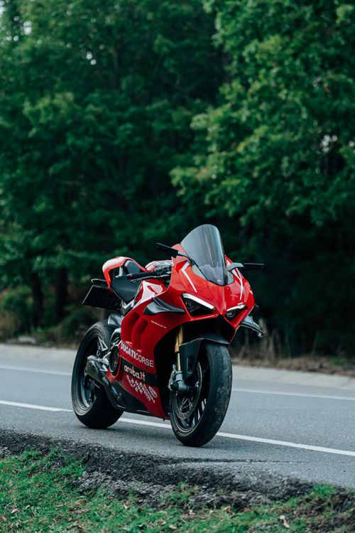 Free Sleek red Ducati motorcycle parked on roadside with lush green trees in the background. Stock Photo