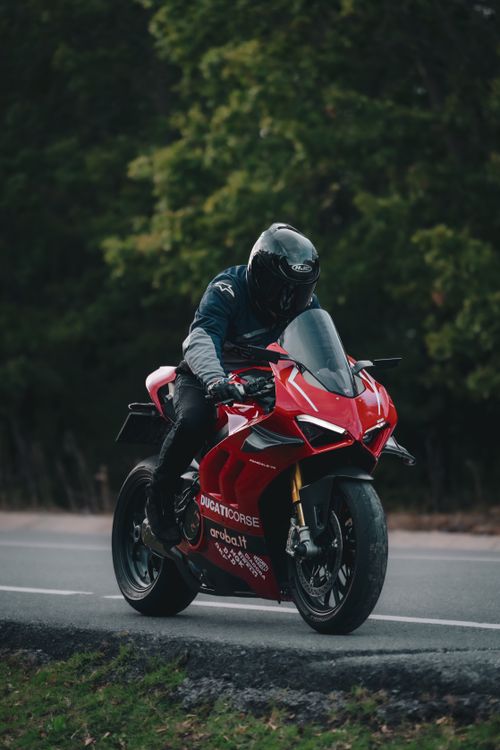Free Dynamic shot of a person riding a red Ducati motorcycle on a scenic road. Stock Photo