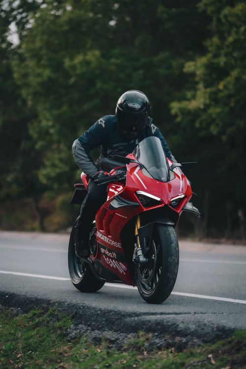 Free A motorcyclist on a red Ducati speeding on a scenic outdoor road against a lush green backdrop. Stock Photo