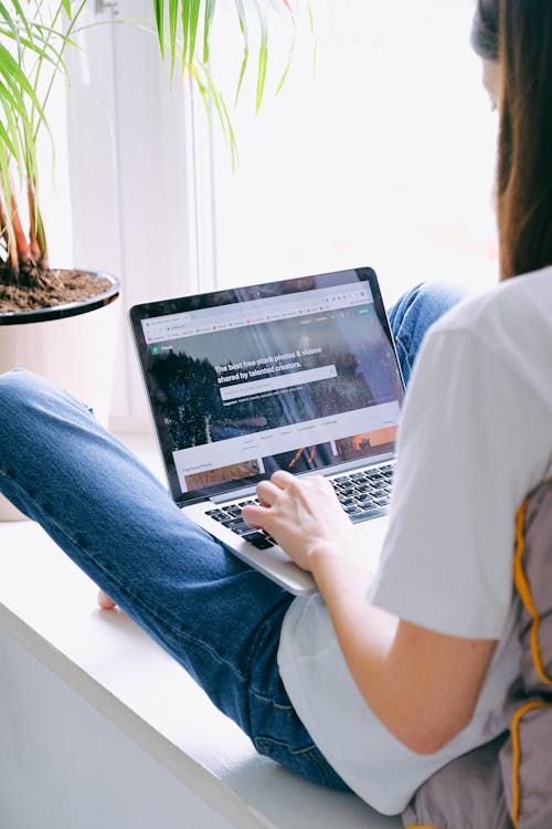 Person in White T-shirt and Blue Denim Jeans Using Laptop