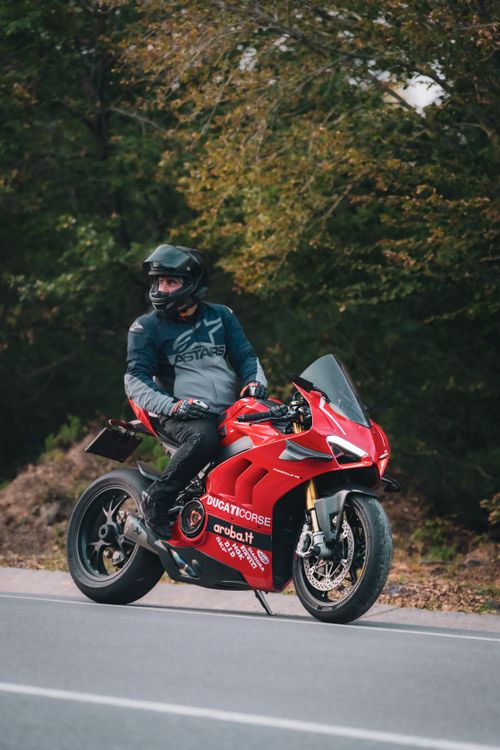 Free A motorcyclist on a red Ducati riding along a scenic road surrounded by lush trees. Stock Photo