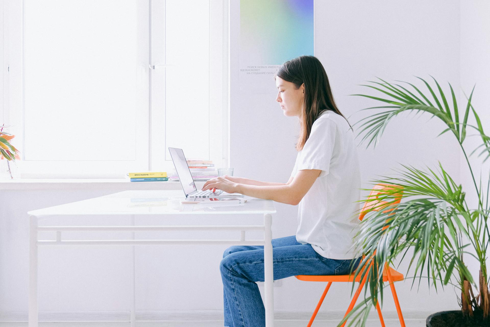 A woman working on a laptop at a bright, minimalist home office with plants.