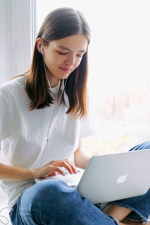 Free Young woman sitting indoors using her laptop and earphones for remote work. Stock Photo