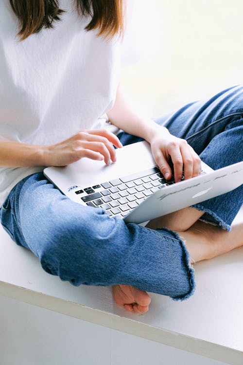 Person in Blue Denim Jeans Using Macbook