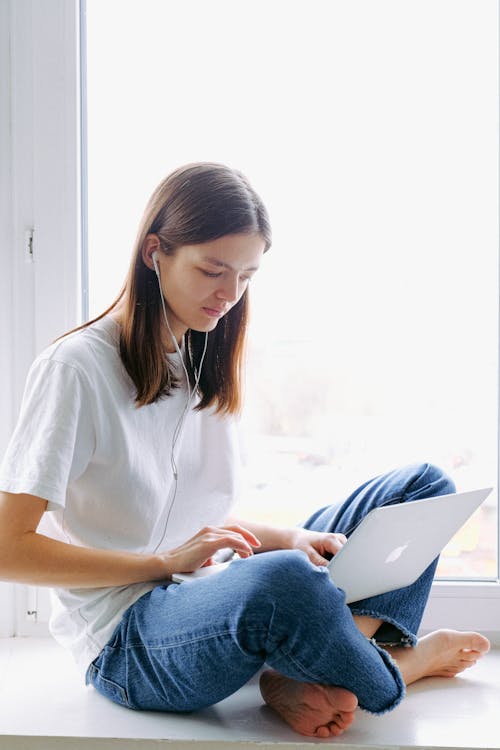 Free Woman In White T-shirt And Blue Denim Jeans Sitting By The Window Stock Photo