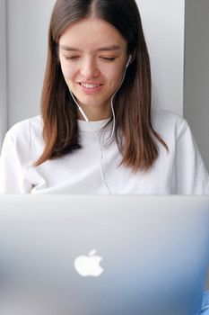 一位年轻女子戴着耳机，在家中使用笔记本电脑