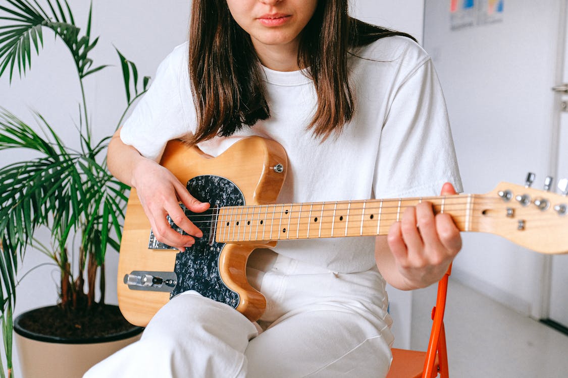 Free A woman in a white outfit playing an electric guitar indoors, enjoying leisure time. Stock Photo