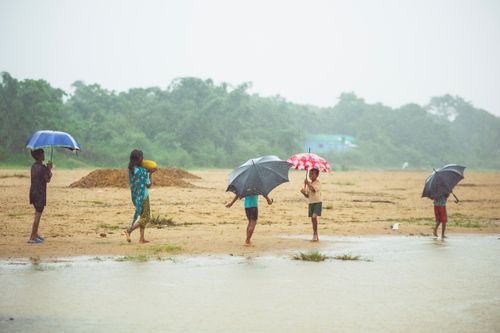 Free Children with umbrellas walk through a rainy field, creating a vibrant monsoon scene. Stock Photo