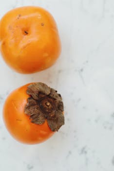 Two ripe persimmons placed on a marble surface, showcasing their vibrant color and natural texture.