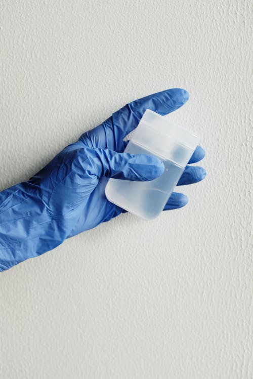 Person in Blue Gloves Holding White Plastic Bottle