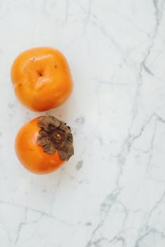 High-angle view of fresh persimmons on a marble surface, showcasing their vibrant color and natural texture.