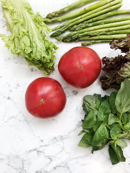Top view of fresh vegetables including asparagus, tomatoes, and lettuce on a marble surface, highlighting healthy eating.