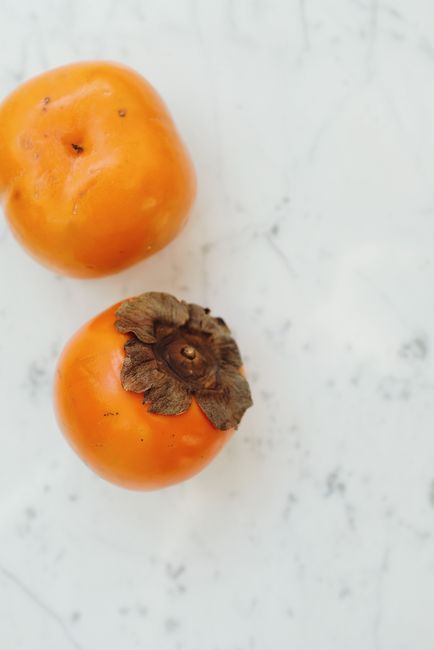 Fresh persimmons on a marble surface, showcasing their vibrant orange hue and delicious ripeness.
