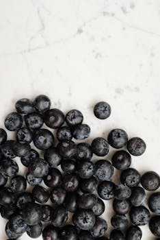 A close-up of fresh and juicy blueberries scattered on a white marble surface.