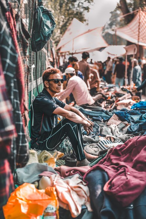 Free Relaxed vendor at bustling outdoor street market, showcasing colorful clothes, a warm atmosphere, and diverse crowd. Stock Photo