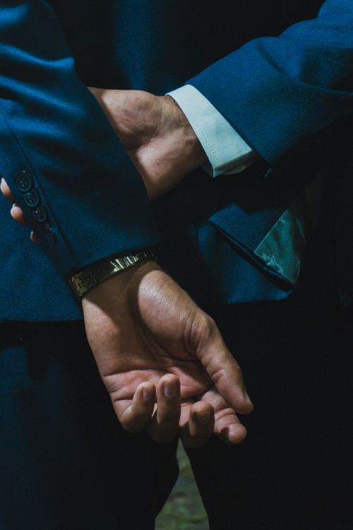 Free Close-up of a man's hands in handcuffs behind his back, dressed in a blue suit. Dramatic lighting enhances the tension. Stock Photo