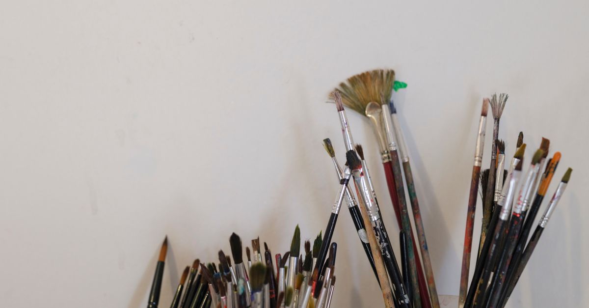 Close-up of various paintbrushes set in holders against a white wall in an artist's workspace.