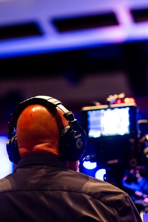 Free A bald male videographer with headphones operating a camera during an indoor event. Stock Photo
