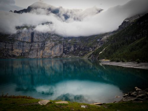 Free Breathtaking view of a serene mountain lake surrounded by rocky cliffs and misty clouds. Stock Photo