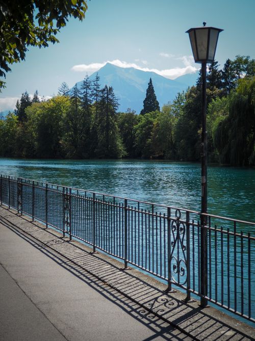 Free Tranquil riverside path with iron railing and scenic mountain views under a clear sky. Stock Photo