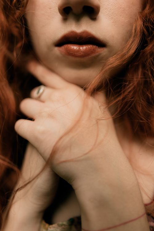 Free Close-up artistic portrait focusing on a woman's lips, hand, and wavy red hair. Stock Photo
