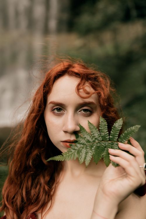 Free Portrait of a redhead woman holding a fern leaf with a blurred natural background. Stock Photo