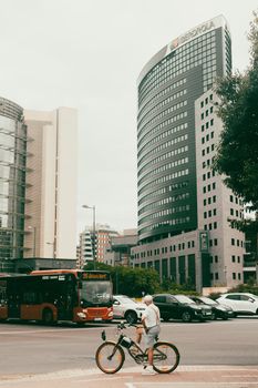 Cyclist pauses at a city intersection with striking modern architecture in the background.