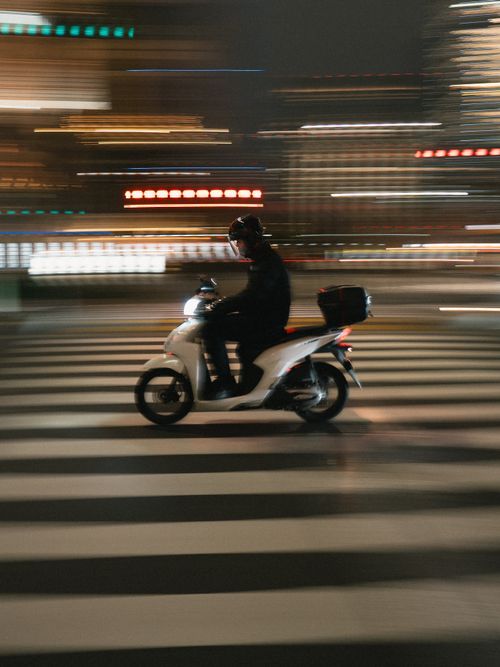 Free Blurred motion shot of a scooter rider crossing city streets at night in Japan. Stock Photo