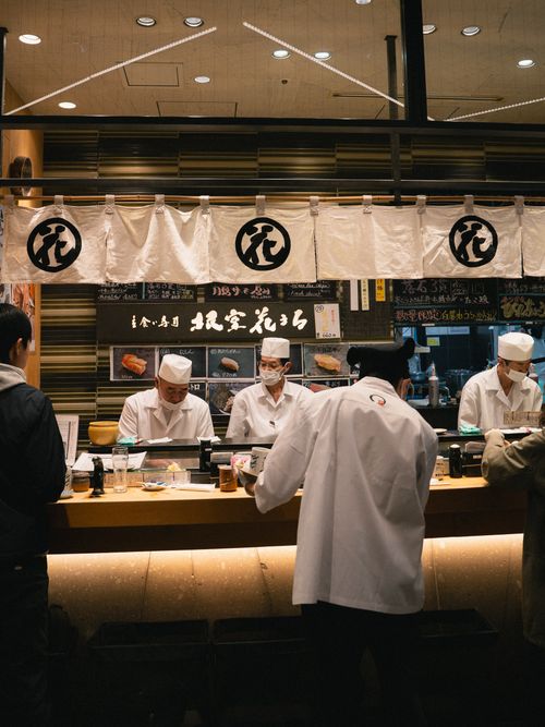 Free Authentic sushi bar in Japan showcasing chefs preparing fresh sushi delicacies. Inviting ambiance with a touch of cultural essence. Stock Photo