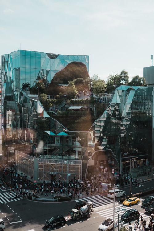 Free A reflective modern glass building with geometric designs in a bustling city street scene. Stock Photo