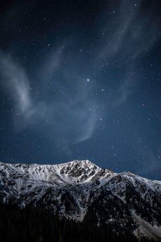A breathtaking view of a snowy mountain range under a star-filled night sky in Kyrgyzstan.