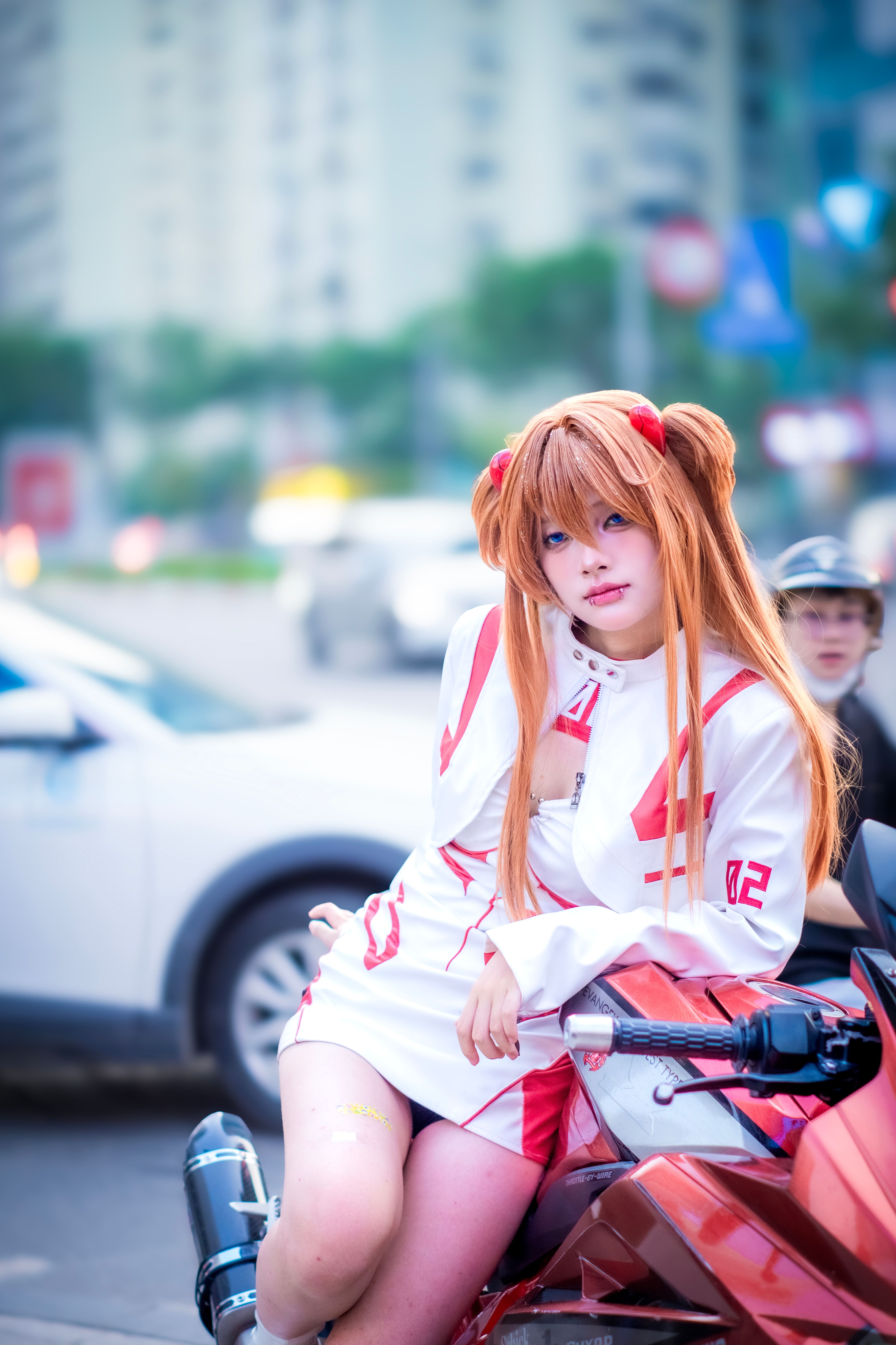 Cosplayer dressed as an anime character on a motorcycle in a city backdrop.