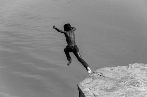 Grayscale Photo of a Child Jumping off a Cliff