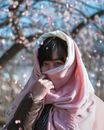 在日本，一位亚洲女性戴着粉红色围巾欣赏樱花