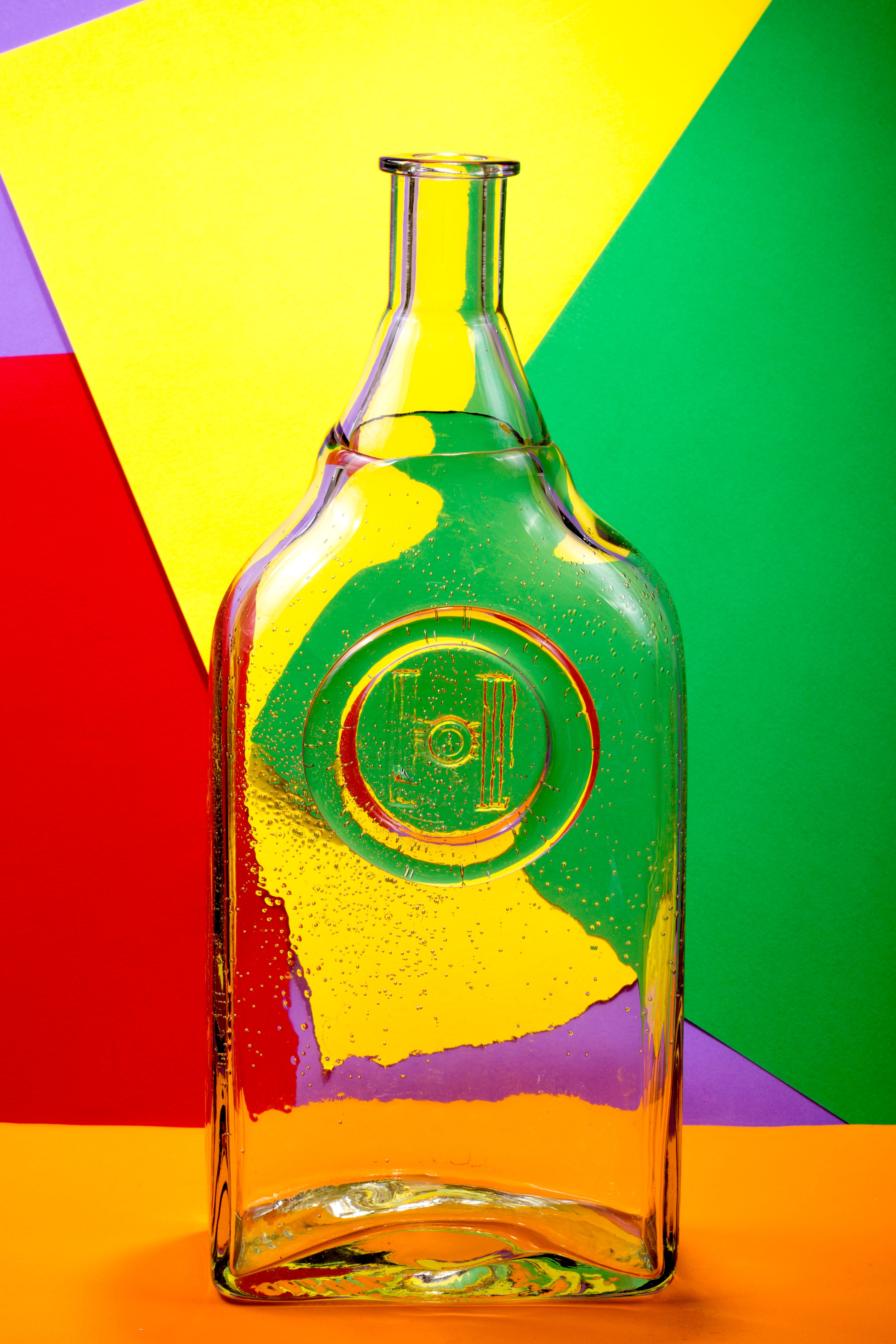 Colorful composition of a transparent glass bottle with vivid paper backdrop.