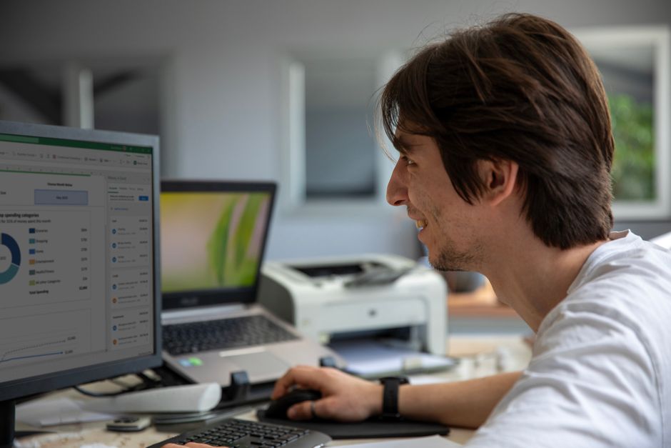 A young professional smiling and working on a desktop computer in a modern office environment.