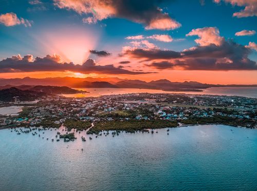 Free A breathtaking aerial view of a coastal town at sunrise with vibrant skies and serene waters. Stock Photo