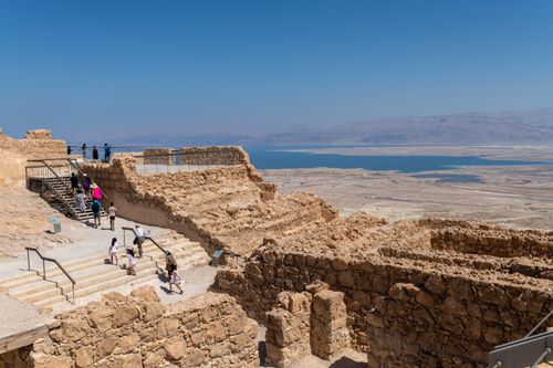 Free Tourists explore the historic ruins of Masada with stunning views of the desert and Dead Sea. Stock Photo