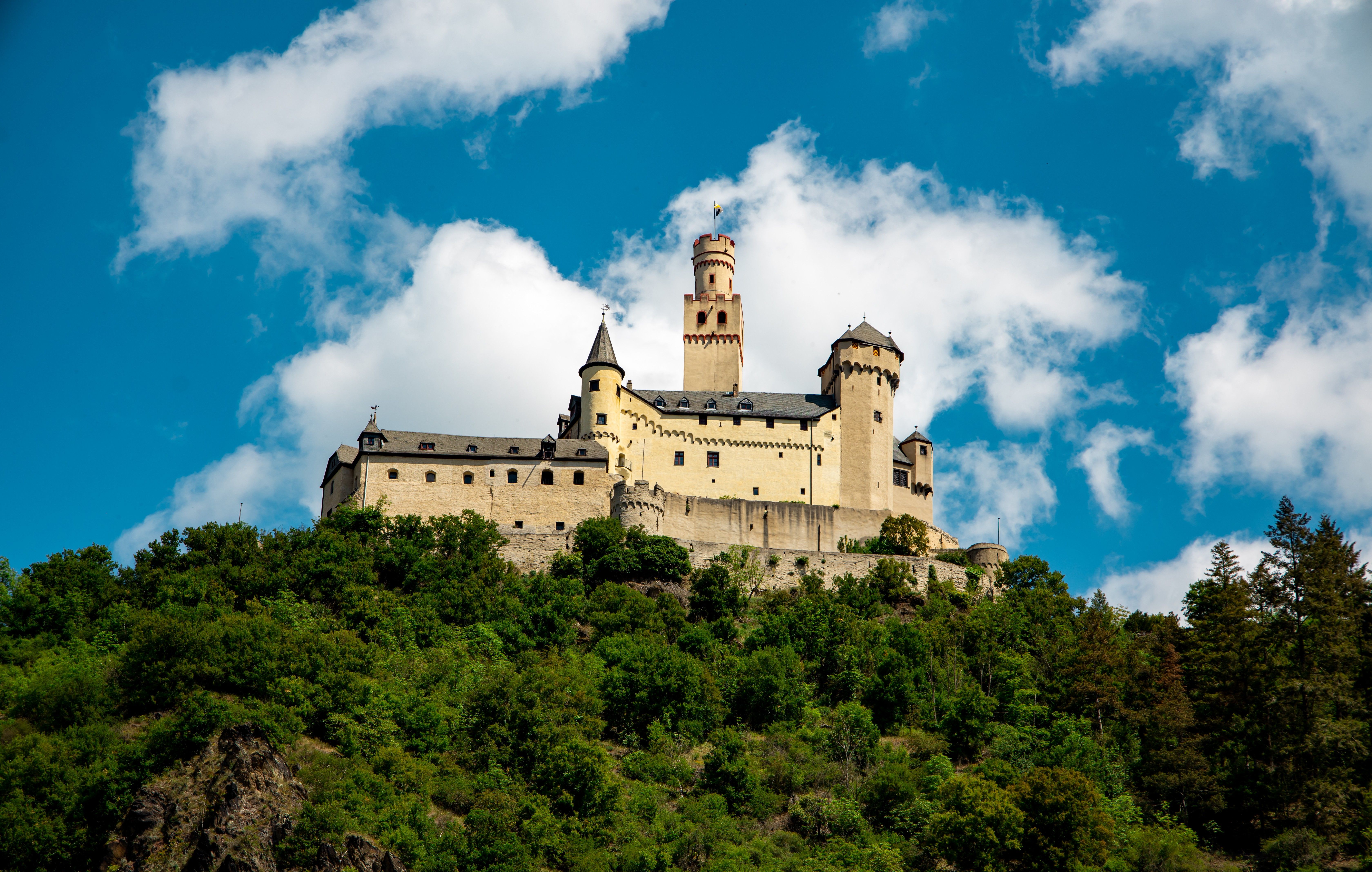 View of Marksburg Castle perched on a lush hill under a vibrant blue sky.