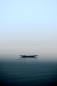 A lone boat floats on misty waters under a soft morning sky, evoking tranquility and solitude.