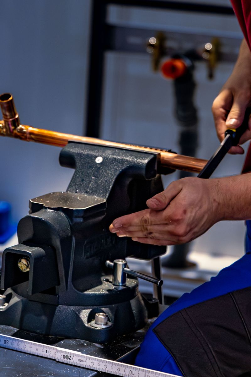 Copper pipe clamped in a bench vise while a plumber works it with a hand tool