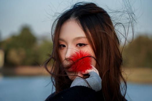 A woman poses with a red feather in a windy outdoor setting.
