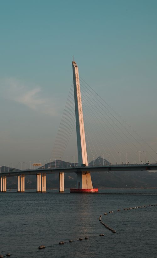 Free Capture of a modern cable-stayed bridge over a river during sunset with mountains in the background. Stock Photo