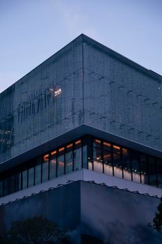 A modern glass building with illuminated windows at dusk, showcasing contemporary architecture.